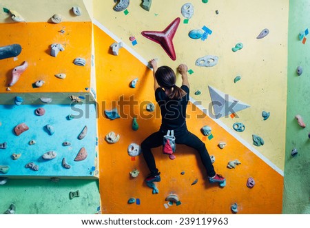 Girl climbing up on practice wall indoor, rear view