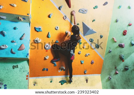 Girl climbing up on practice wall in gym, rear view