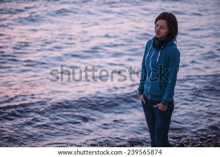 Young woman with big headphones walking on coast and enjoying view of sea in the evening