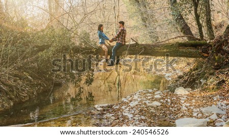 Traveler young couple in love sitting on fallen tree trunk over the river in autumn forest