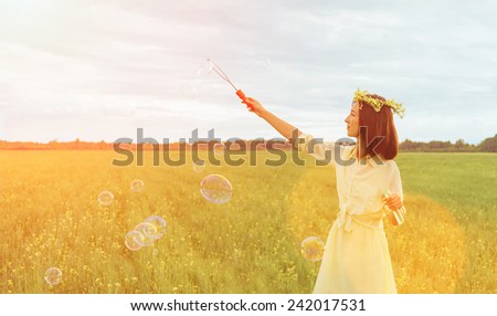 Beautiful young woman blowing soap bubbles on summer meadow at sunny day. Image with sunlight effect