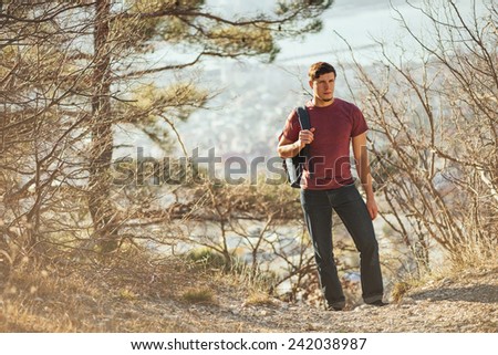 Young hiker man with backpack walking in forest. Hiking and recreation theme