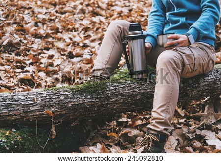 Hiker young woman holding a cup of tea or coffee and thermos in autumn forest. Hiking and leisure theme
