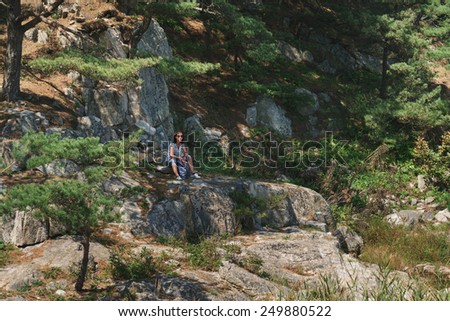 Hiker young woman with backpack resting on stone rock in summer outdoor