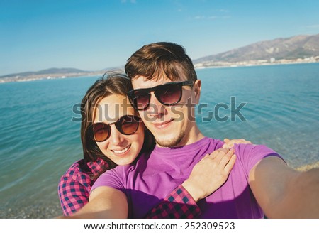 Happy young couple in love taking photographs self-portrait on beach on background of blue sea