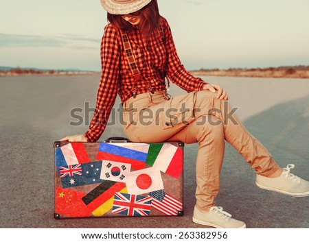 Traveler young woman sitting on suitcase. Suitcase with stamps flags of different countries. Concept of travel
