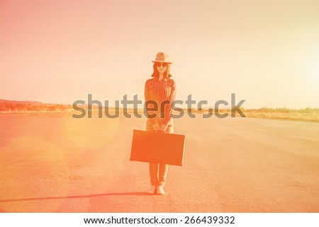 Traveler hipster woman stands on road with vintage suitcase, space for text. Image with sunlight effect