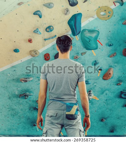 Young man standing in front of a practical climbing wall indoor and preparing to climb
