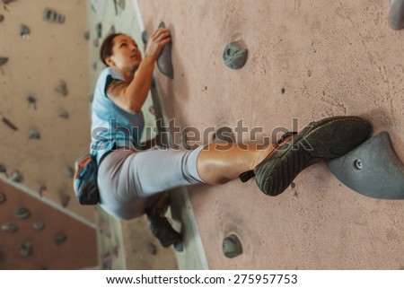 Free climber young woman climbing on practical wall indoor, bouldering