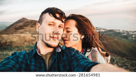 Happy young loving couple taking self-portrait on peak of mountain outdoor