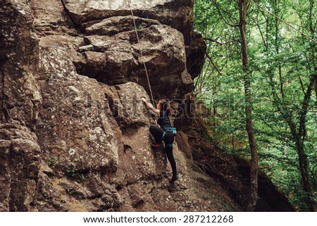 Sporty young woman wearing in safety equipment climbing on stone rock outdoor in summer, side view