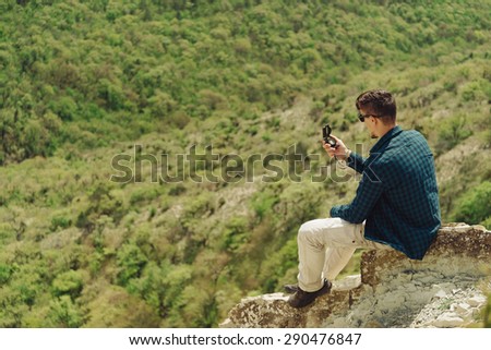 Traveler young man sitting on stone in the mountains and searching direction with a compass in summer