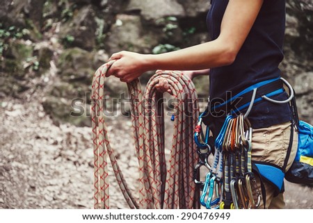 Climber woman wearing in safety harness with equipment holding rope and preparing to climb