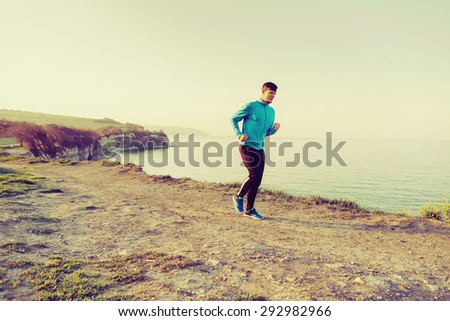 Sporty young man running on coast near the sea in summer in the morning. Concept of sport and healthy lifestyle