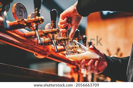 bartender hand at beer tap pouring a draught beer in glass serving in a bar or pub Сток-фото © 