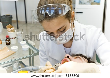 Young female dentist in her clinic with patient laying on chair