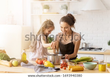 Mother and daughter preparing tasty food at kitchen. Mommy teaching lovely kid to cook. Happy smiling mom and loving child spending time together at home. Healthy meal and dinner preparation