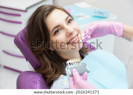 Dentist choosing teeth enamel shade color for young smiling female patient before whitening procedure. Happy woman with beautiful white smile on stomatological appointment. Dentistry and stomatology. Stockfoto © 