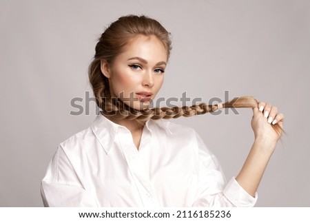 Glamourous young blond caucasian girl with healthy shiny long hairs in pigtail hold braid in hand. Alluring female with stylish plait posing on gray studio background. Haircare treatment cosmetics ad Stock foto © 