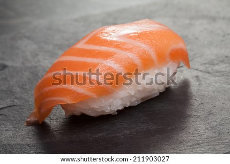 Japanese dish of sushi rice with salmon on matte black background close-up.