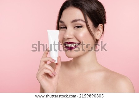 Smiling young girl holding cosmetics mockup tube, facial cream template jar. Pretty woman with healthy glowing skin, perfect makeup, bare shoulders advertise natural skincare or make-up beauty product Foto stock © 