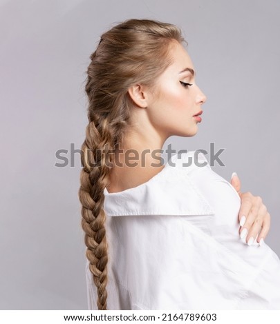 Glamourous young blond caucasian woman with healthy shiny long hairs in pigtail hold braid in hand. Alluring female with stylish plait posing on gray studio background. Haircare treatment cosmetics ad Foto stock © 