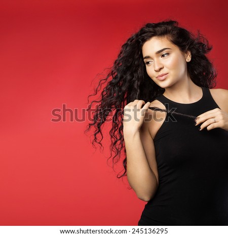 Beautiful young woman with dark flowing curly hair and perfect skin on a red background