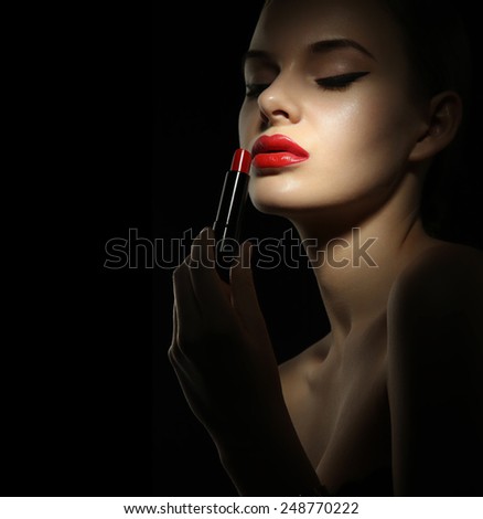 Beautiful woman with perfect skin paints her lips red lipstick . Blonde with blue eyes and red lips on a black background.