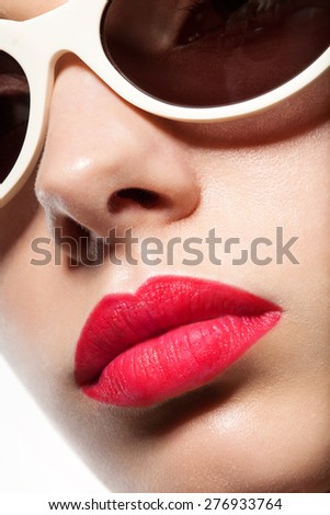 A woman\'s face close up in sunglasses and red lips on a white background