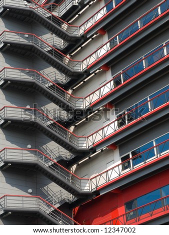 Red and grey coloured metal staircase going up the side of a shopping centre building on the outside