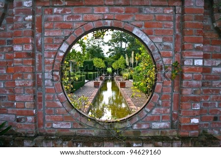 A peak through an antique brick wall into a private garden and water area with beautiful landscaping in South Island, New Zealand.