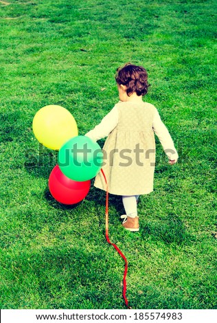 Alone child with balloons walking on the green grass.
