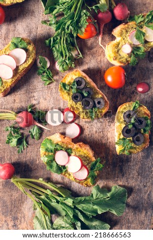 Bruschettas with pesto sauce and vegetables on the wooden background from above
