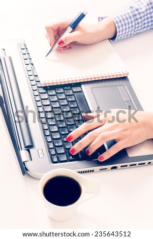 Female typing on laptop keyboard and writing on blank paper,selective focus