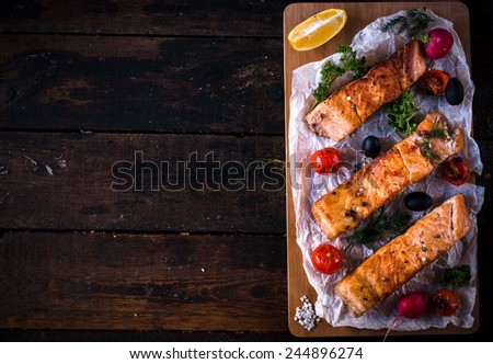 Prepared salmon fish fillets and grilled tomato on wooden background with blank space