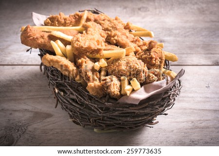 Wooden basket stuffed with fried chicken and French fries,selective focus