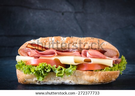 Big ciabatta sandwich with meat and cheese on dark background
