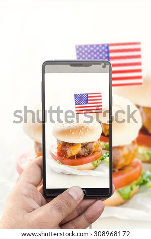 Man photographing with his cell phone camera big beef burgers with American flag