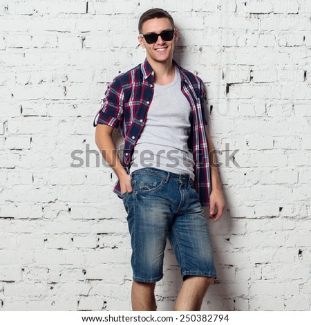 Handsome stylish young man in jeans shorts and shirt. Attractive hipster  with a bristle,sunglasses.