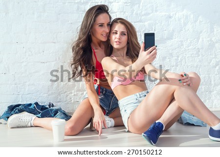 two women friends taking selfie together wearing red bikini swimsuit summer sunny day jeans shorts jeanswear street urban casual style having fun