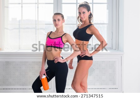 Two young sportive active fit and slim beautiful woman posing in sportswear indoors with the window.