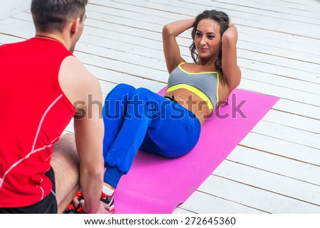 athletic sporty couple friends. Woman doing crunches abdominal exercises on floor in gym with a help of guy concept training exercising workout fitness aerobic.