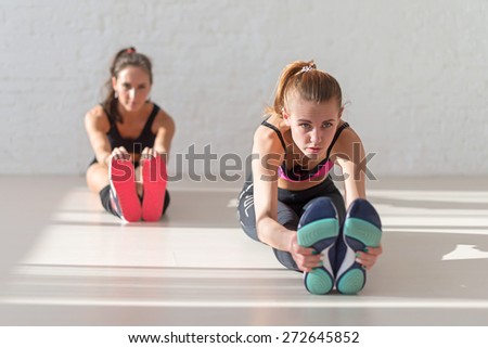 Two young women stretching seated forward bend warm up at gym fitness, sport, training and lifestyle concept.