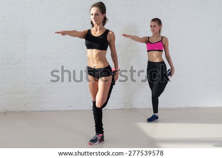 women doing stretching exercises warm up standing on one leg outstretched arm in front of her.