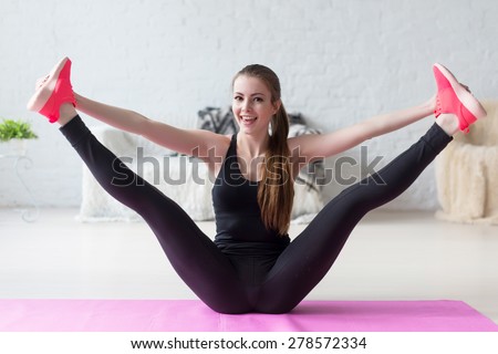 Funny smiling girl holding legs apart doing exercises aerobics warming up with gymnastics for flexibility leg stretching workout at home fitness
