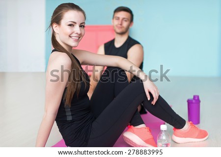 sporty couple friends athletic woman and man sportsmen in sport gym sitting floor looking at camera.
