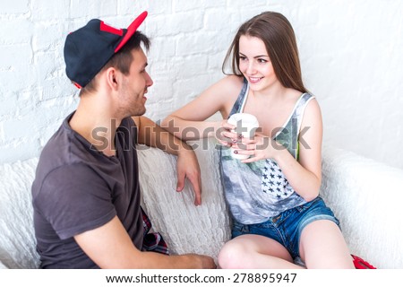 Friends girl with cup of coffee and guy sitting on sofa at home in summer jeanswear street urban casual style talking, having fun.