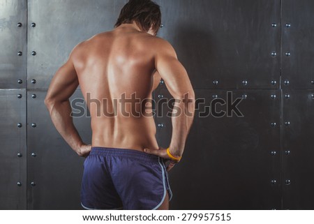 Athletic young man showing muscles of back Rear view of strong young male. Fitness male model standing near wall healthy lifestyle bodybuilding concept.