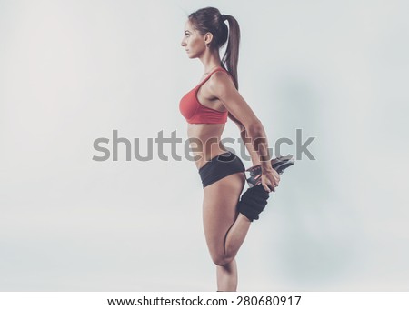 Muscular active athlete woman standing looking forward leg in hands doing exercise warming up working stretching fitness, sport, training and lifestyle concept