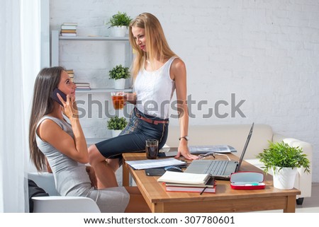 businesswoman sitting on table with cup of coffee communicating with her colleague in office